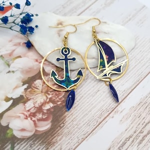 Peut inclure: Une paire de boucles d'oreilles créoles dorées avec un ancre bleue et un pendentif de voilier bleu. Les breloques sont entourées d'un cercle doré et ont un pendentif en forme de larme bleue.