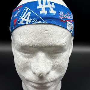 Pode incluir: Uma faixa azul com o logotipo e o nome da equipa dos Los Angeles Dodgers em branco e vermelho. A faixa é exibida numa cabeça de manequim branca.