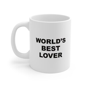 Puede incluir: Taza de café de cerámica blanca con texto negro que dice "WORLD'S BEST LOVER".