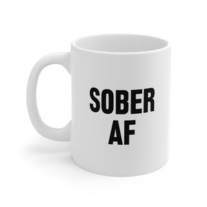 May include: White ceramic coffee mug with black text that reads "SOBER AF".