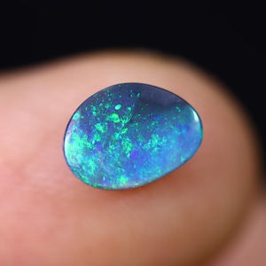 May include: A dark blue and green opal gemstone with a teardrop shape. The opal has a bright, iridescent sheen.