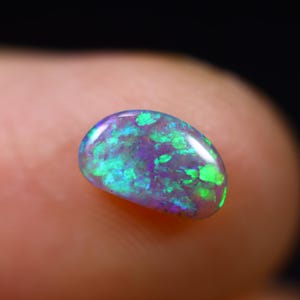 Könnte beinhalten: Ein grüner und violetter Opal-Edelstein mit einer glatten, ovalen Form. Der Opal hat einen leuchtenden, irisierenden Glanz.