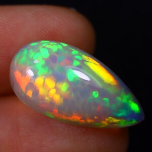 May include: A teardrop-shaped opal gemstone with a white body and iridescent flashes of green, yellow, orange, and red.
