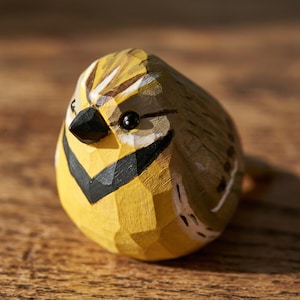 Close-up of a hand-carved wooden Western Meadowlark figurine, highlighting the faceted whittled texture and hand-painted yellow plumage. The bird sculpture is shown from a side profile, showcasing its artisanal craftsmanship. Perfect for rustic home decor, a nature-themed shelf sitter, or a unique gift for bird watchers.