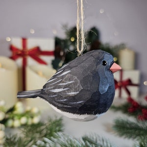 May include: A hand-carved wooden bird ornament with a black and white painted design. The bird has a small, pink beak and is hanging from a twine string.