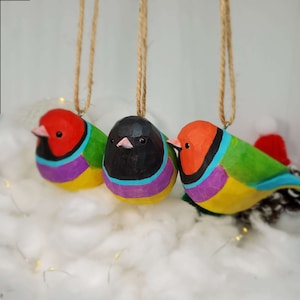 May include: Three wooden bird ornaments with colorful paint and string hangers. The birds are red, black, and green with yellow and purple accents.