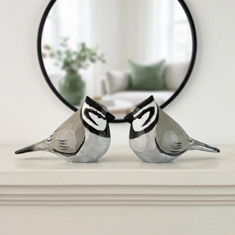 Two hand-painted Bridled Titmouse wooden bird sculptures facing each other on a mantel. Basswood figurine home decor for bird watchers.