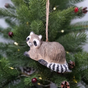 K&ouml;nnte beinhalten: Ein h&ouml;lzerner Waschb&auml;r-Anh&auml;nger mit braunem und grauem K&ouml;rper und einem schwarz-wei&szlig; gestreiften Schwanz. Der Anh&auml;nger h&auml;ngt an einer braunen Schnur.