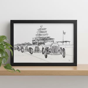 May include: A black framed print showing a pen and ink drawing of classic race cars in front of a multi-tiered structure. The artwork is displayed on a light wood shelf with a potted plant.