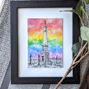 May include: A framed watercolor painting of a monument with a rainbow sky in the background. The monument is a tall, slender tower with a statue on top. The rainbow sky is a vibrant mix of red, orange, yellow, green, blue, indigo, and violet.