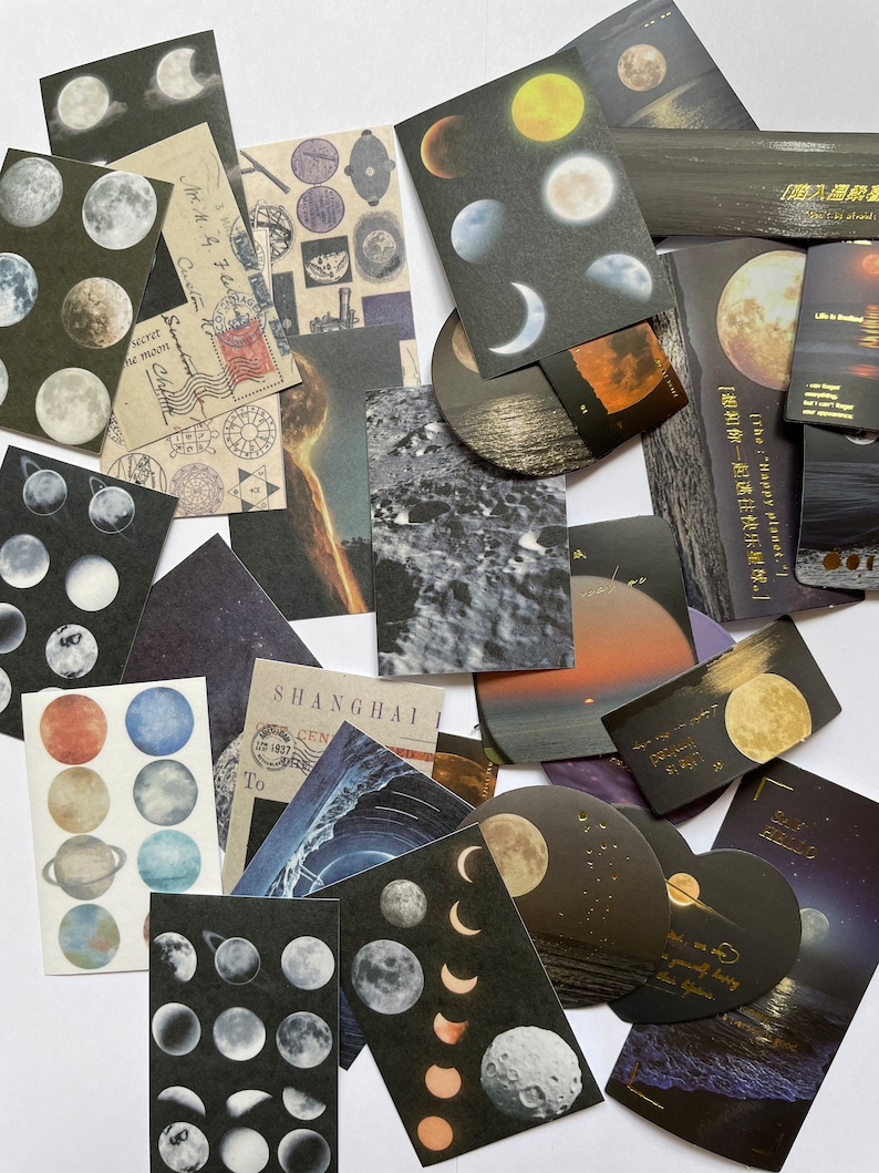May include: A collection of decorative paper ephemera featuring celestial and landscape designs. The assortment includes stickers and cards with images of moons, planets, and ocean scenes. Some cards have text in English and Chinese.