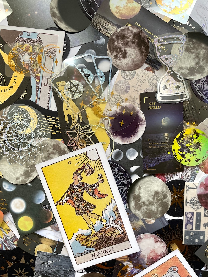 May include: A collection of celestial-themed stickers and cards. The image features moon-shaped stickers, tarot cards, and other decorative elements with gold foil accents. The tarot card shows a figure with a dog, the word "NEBUNUL" is visible.