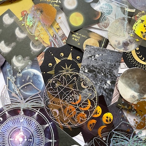 May include: A collection of celestial-themed stickers and ephemera. The assortment includes various shapes and sizes, featuring moons, stars, and astrological symbols. Some stickers have holographic and glitter accents, with text that reads "Life is limited".