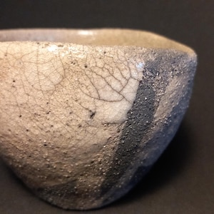 Puede incluir: Un cuenco de cerámica hecho a mano con una superficie texturizada única. El cuenco presenta una mezcla de colores, incluyendo blanco roto, gris y azul oscuro, con un aspecto agrietado y envejecido. El diseño del cuenco es asimétrico, lo que aumenta su atractivo artístico.