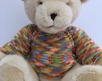 May include: A cream-colored plush teddy bear wearing a multi-colored striped sweater. The sweater has shades of orange, green, blue, and white.