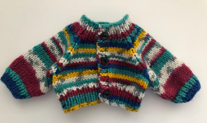 May include: A colorful, hand-knitted cardigan with horizontal stripes in teal, burgundy, yellow, and white. The sweater has a round neckline, long sleeves, and is fastened with three black buttons. The garment is made of thick yarn.