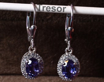 Puede incluir: Un par de pendientes colgantes de plata con una piedra ovalada púrpura rodeada por un halo de piedras pequeñas transparentes. Los pendientes cuelgan de una tarjeta blanca con la palabra "Tresor" impresa en ella.