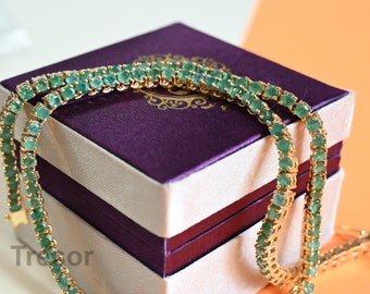 Op de afbeelding: Twee tennisarmbanden met smaragdgroene edelstenen op een witte en paarse doos met het woord "Tresor" gedrukt op de bodem.