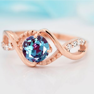 May include: A rose gold ring with a blue and purple gemstone and smaller clear gemstones. The ring has a twisted band design and the word "Tresor" is visible on the band.