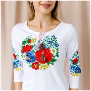 May include: White long-sleeved shirt with a colorful floral embroidery design. The embroidery features red, blue, yellow, and green flowers.