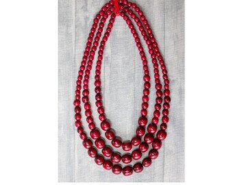 May include: A three-strand necklace made of dark red wooden beads. The beads are round and have a smooth, polished finish.