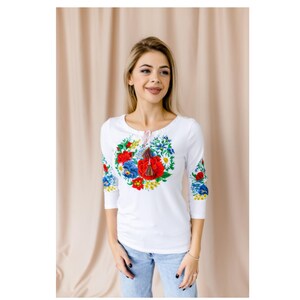 May include: White long-sleeved shirt with a floral embroidery design in red, blue, and yellow. The embroidery features a large bouquet of flowers with a red poppy in the center.