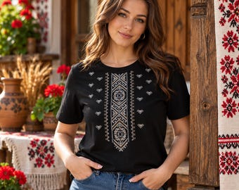 May include: A black short-sleeved t-shirt featuring a central vertical panel of intricate white and grey geometric embroidery patterns, complemented by smaller matching embroidered motifs scattered across the chest area.