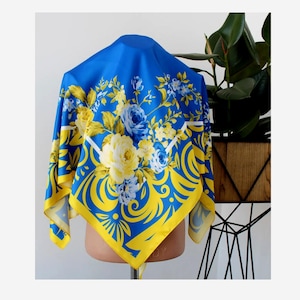 May include: A blue and yellow floral patterned square scarf. The scarf has a yellow border and a floral design with yellow, blue, and white flowers.