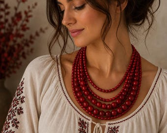 May include: A multi-strand necklace featuring five layers of glossy, deep red spherical beads of varying sizes. The beads are strung in a graduated pattern, with the smallest beads at the top and the largest beads at the bottom, creating a layered effect.