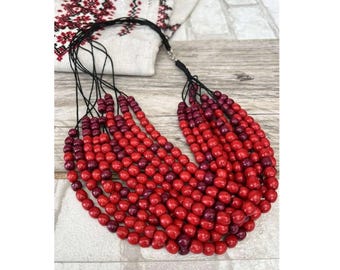 May include: A multi-strand necklace made of red and burgundy wooden beads. The necklace is layered and has a cascading effect.