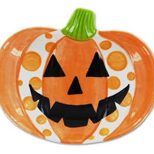 Puede incluir: Plato de calabaza de cer&aacute;mica naranja y blanco con una cara de calabaza negra y lunares naranjas.