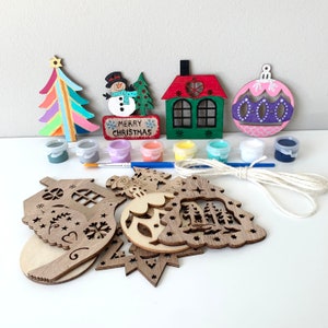 May include: A Christmas ornament craft kit with wooden ornaments, paint, and twine. The ornaments include a house, a tree, a snowman, a star, and a ball. The paint colors are blue, green, yellow, red, white, and pink. The kit includes the text "Merry Christmas".