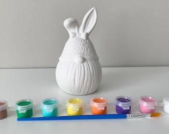 May include: A white ceramic bunny figurine with a bow tie, ready to be painted. The set includes six small paint pots in brown, green, blue, yellow, orange, and purple, along with a paintbrush.