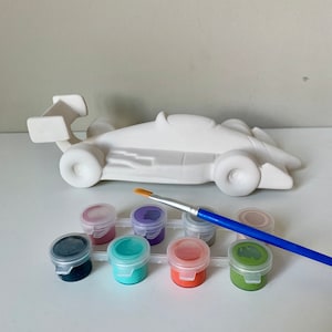 May include: A white ceramic race car figurine with a paintbrush and eight small paint pots in various colors, including black, purple, pink, teal, green, and orange.