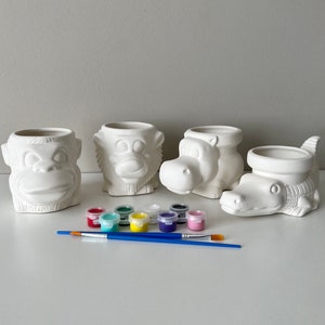 May include: Four ceramic animal planters, a monkey, a hippopotamus, a crocodile, and a bear, with a set of ten paint pots in various colors. The planters are ready to be painted.