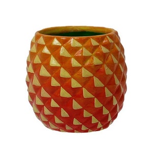 Puede incluir: Maceta de cer&aacute;mica en forma de pi&ntilde;a naranja y amarilla con un patr&oacute;n geom&eacute;trico.