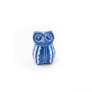 May include: A small ceramic owl figurine featuring a vibrant blue glaze with hand-painted white details. The owl has large circular eyes and a body decorated with vertical scalloped white stripes that extend from the chest to the base.
