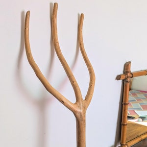 Könnte beinhalten: Ein Holzrechen mit drei Zinken, der Stiel ist aus einem Stück Holz gefertigt und hat eine natürliche Oberfläche.