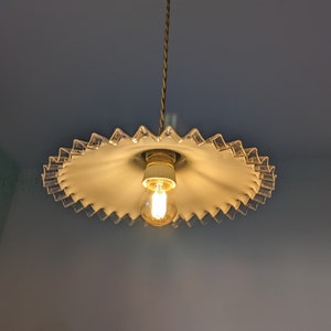 May include: A white glass lampshade with a scalloped edge hangs from a ceiling. The lampshade has a single light bulb inside.