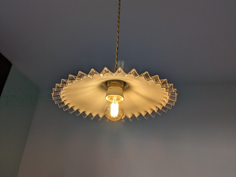May include: A white glass lampshade with a scalloped edge hangs from a ceiling. The lampshade has a single light bulb inside.