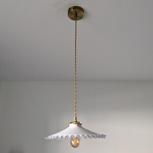 May include: A white pendant light with a scalloped edge shade and a gold cord hanging from a gold ceiling fixture.