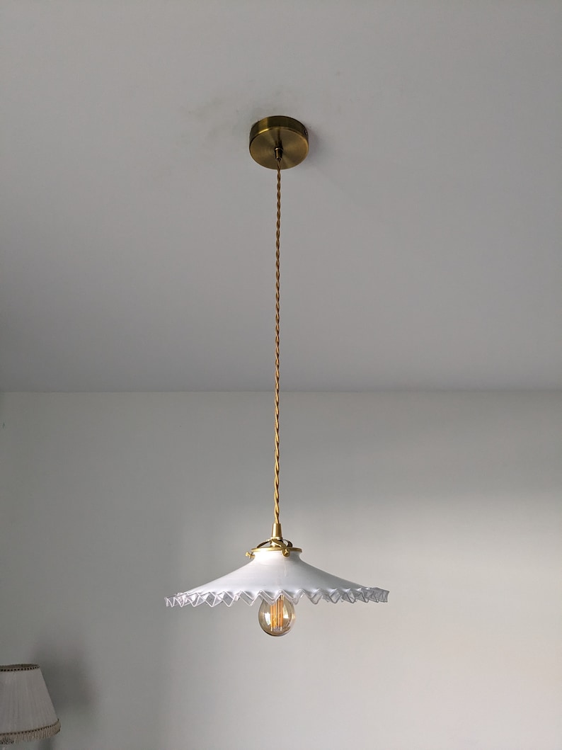May include: A white pendant light with a scalloped edge shade and a gold cord hanging from a gold ceiling fixture.