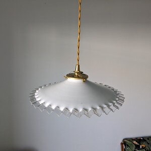 May include: A white pendant light with a scalloped edge and a gold metal fixture.