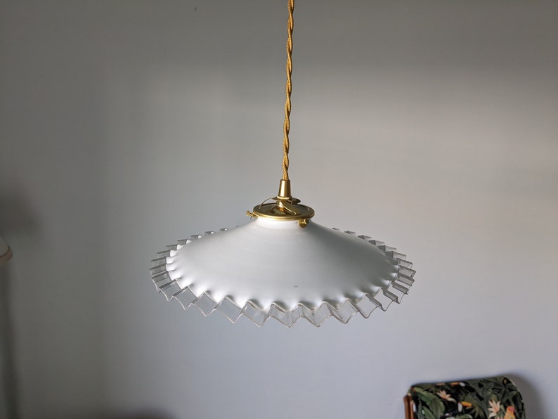 May include: A white pendant light with a scalloped edge and a gold metal fixture.