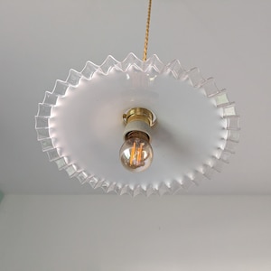 May include: A white ceiling light fixture with a clear glass shade that has a scalloped edge. The light fixture has a single light bulb.