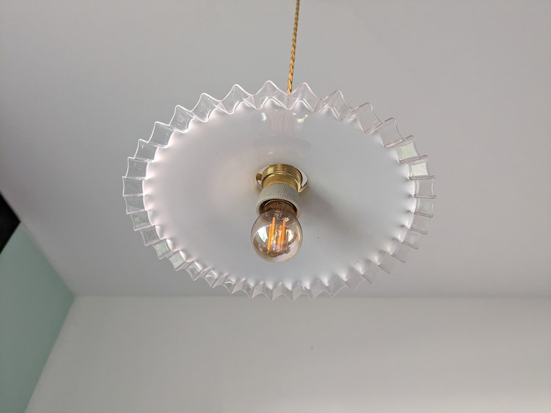 May include: A white ceiling light fixture with a clear glass shade that has a scalloped edge. The light fixture has a single light bulb.