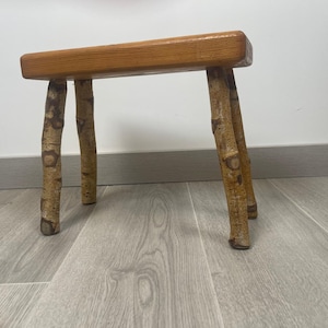 May include: A wooden stool with a natural wood top and four legs made from birch branches.