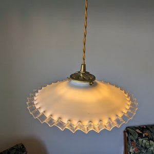 May include: A white glass pendant light fixture with a ruffled edge and a gold metal hanging cord.