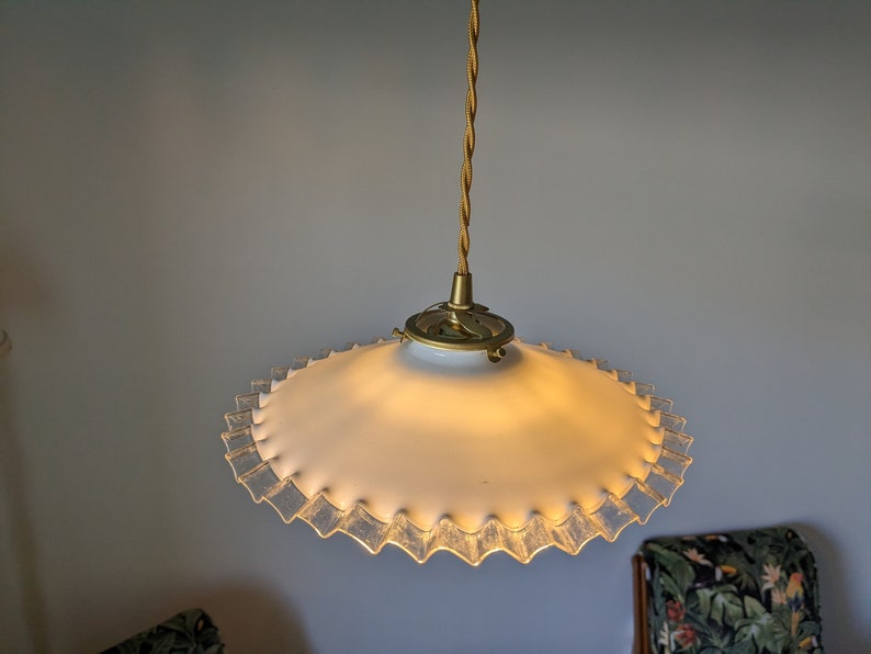 May include: A white glass pendant light fixture with a ruffled edge and a gold metal hanging cord.
