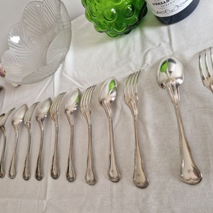 May include: A set of silver cutlery, including forks, spoons, and a ladle, laid out on a white tablecloth.